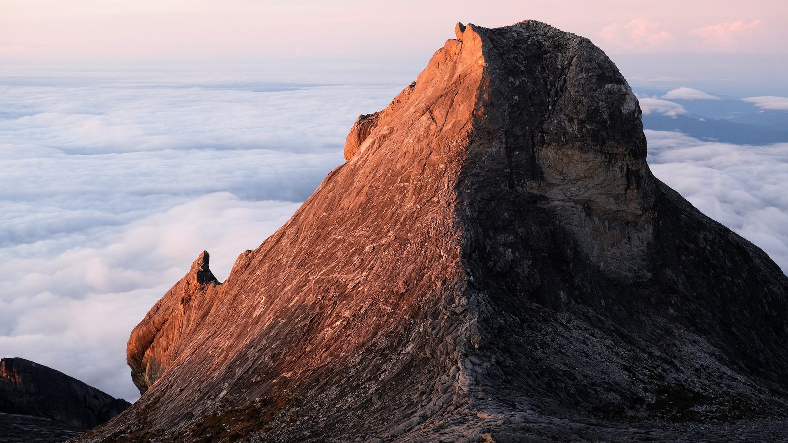 Mount Kinabalu Climb: St John's Peak glowing at sunrise above a sea of clouds on the granite summit plateau, Kinabalu Park, Sabah, Malaysia